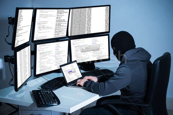 Hacker Using Laptop Against Multiple Monitors At Desk Stock photo © AndreyPopov