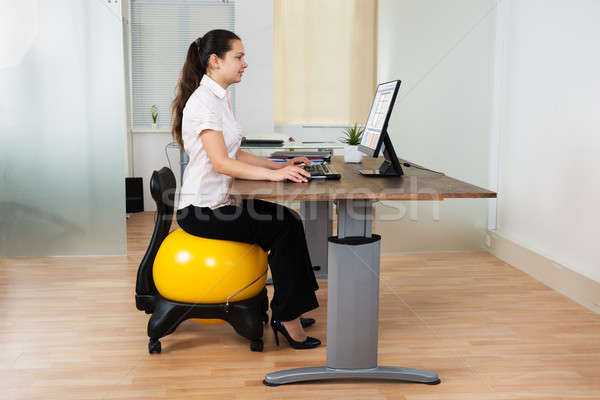 Businesswoman Sitting On Fitness Ball With Computer At Desk Stock