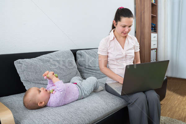 Kadın dizüstü bilgisayar kullanıyorsanız oturma kanepe bebek oynama Stok fotoğraf © AndreyPopov