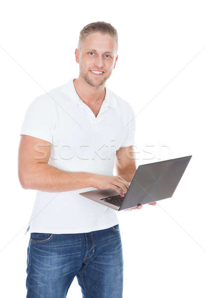 Smiling man in jeans standing using a handheld laptop computer Stock photo © AndreyPopov