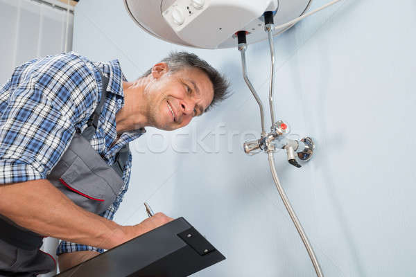 Plumber With Clipboard Looking At Electric Boiler Stock photo © AndreyPopov