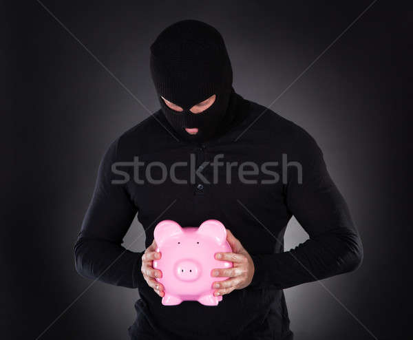Stock photo: Burglar stealing a pink piggy bank