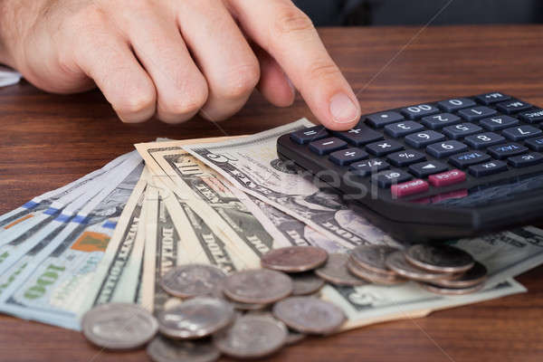 Stock photo: Businessman Using Calculator With Coins And Banknotes On Desk