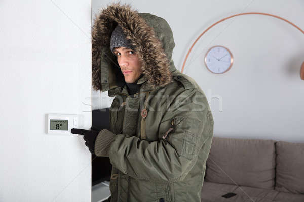 Stock photo: Man In Warm Clothing Pointing To Current Room Temperature