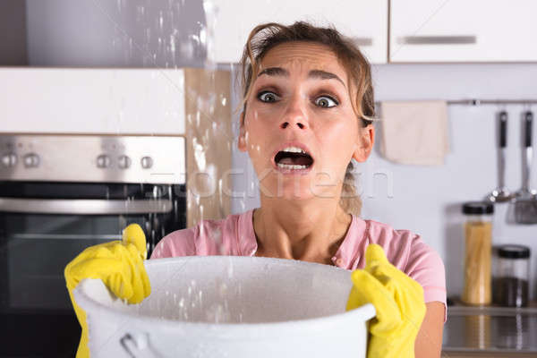Woman Holding A Bucket While Water Droplets Leak From Ceiling Stock photo © AndreyPopov