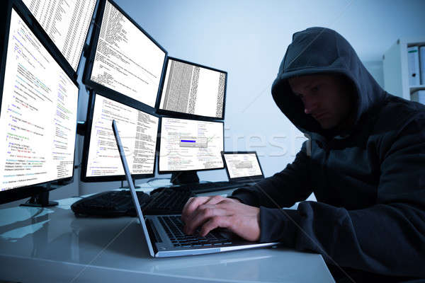 Hacker Using Laptop Against Multiple Monitors At Desk Stock photo © AndreyPopov