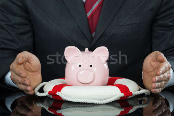 Close-up Of Businessman Hand Protecting Piggybank With Lifebelt Stock photo © AndreyPopov