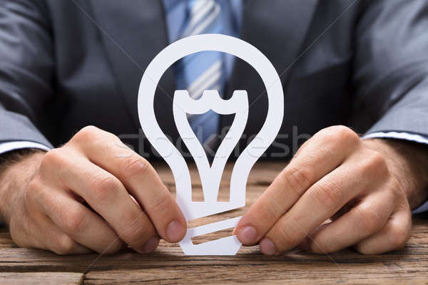 Stock photo: Businessman Holding Paper Light Bulb At Table