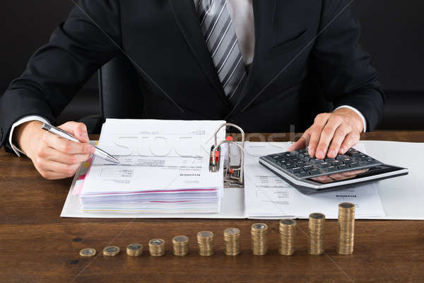 Businessman Calculating Invoice With Coins At Desk Stock photo © AndreyPopov