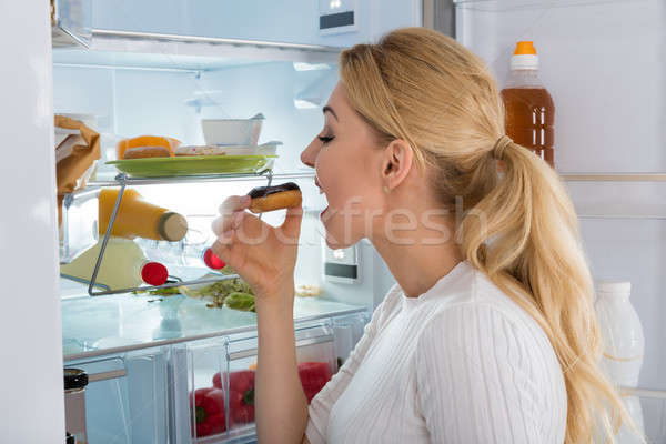 Jeune femme manger donut plaque permanent réfrigérateur Photo stock © AndreyPopov