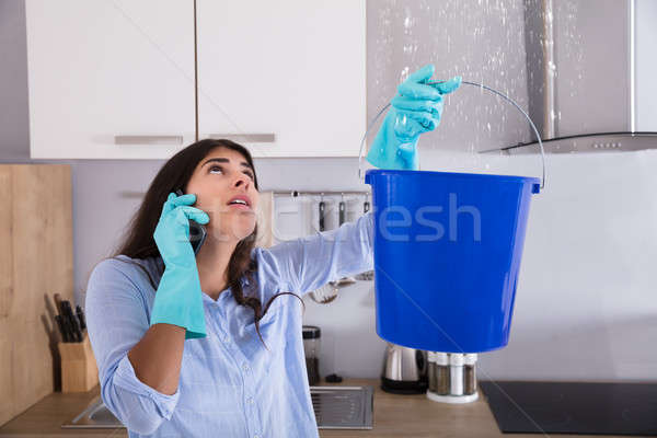 Stock photo: Woman Calling Plumber While Collecting Water