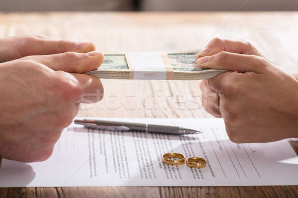 Couple's Hand Holding Currency Over The Divorce Agreement Stock photo © AndreyPopov