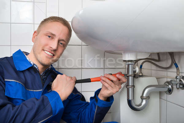 Stock photo: Male Plumber Fixing Sink In Bathroom