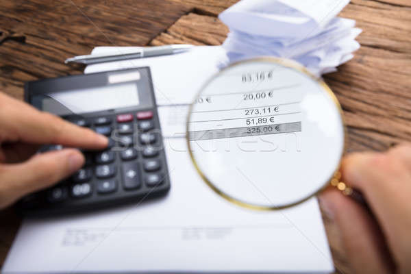 Businessman Examining Invoice With Magnifying Glass At Table Stock photo © AndreyPopov