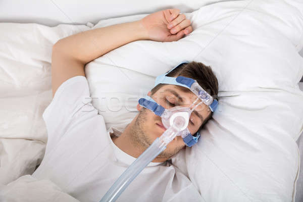 Man Lying On Bed With Sleeping Apnea And CPAP Machine Stock photo © AndreyPopov