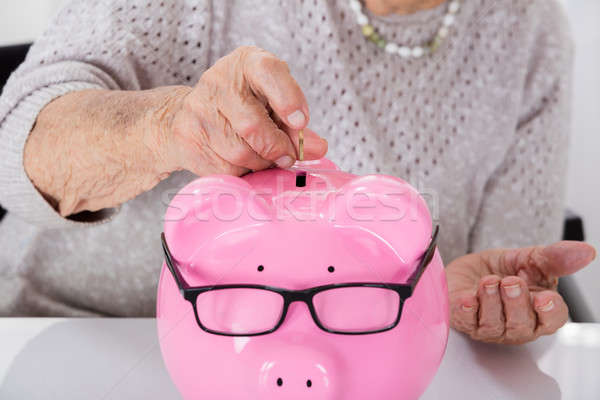 Stock photo: Senior Woman's Hand Inserting Coin In Piggybank