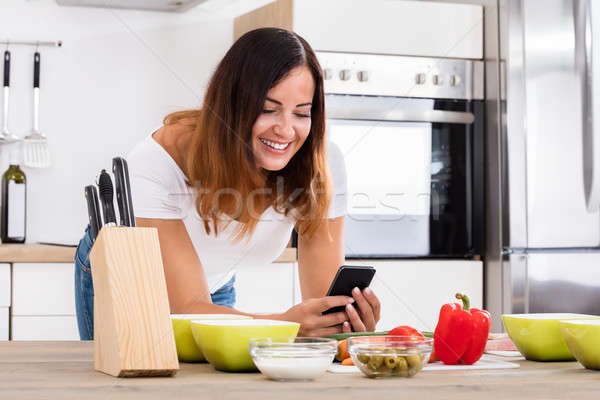 Smiling Woman Using Smartphone In Kitchen Stock photo © AndreyPopov