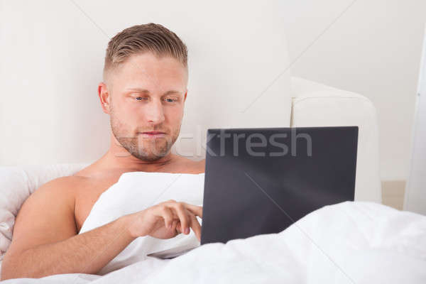 Man sitting up in bed working on a laptop Stock photo © AndreyPopov