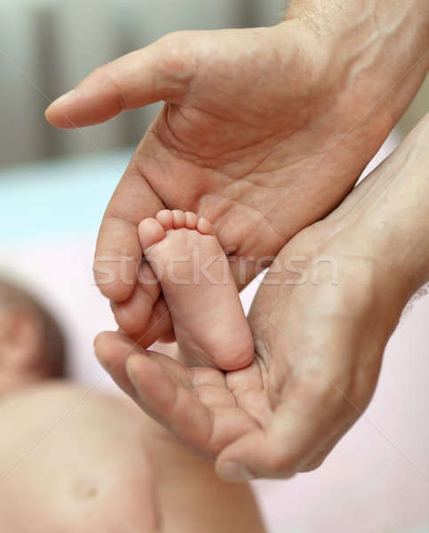 Stock photo: The little baby's legs in the hands of the big daddy
