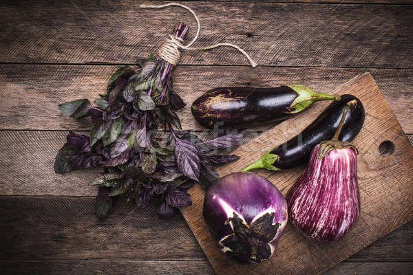 Aubergines and basil on chopping board in rustic style Stock photo © Arsgera