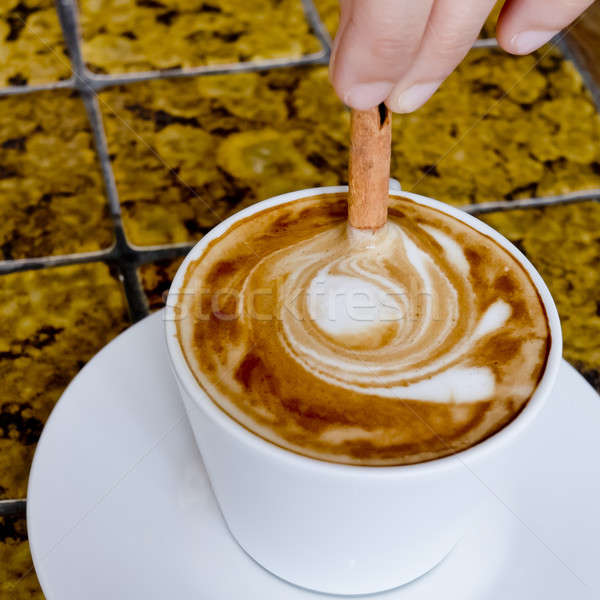 Stock photo: A coffee cup Latte being stirred by Cinnamon sticks.