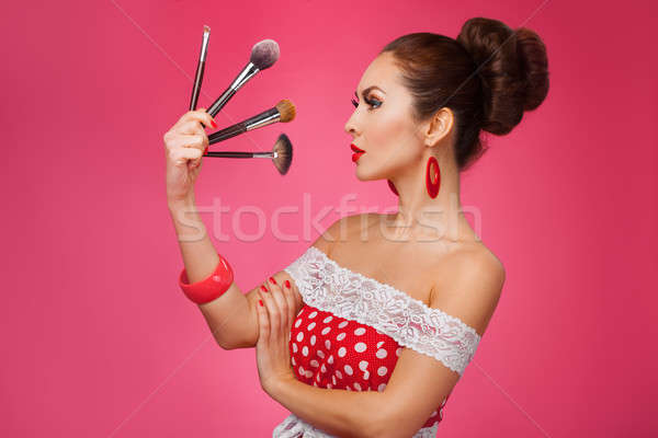 Woman with makeup brushes.   She is standing against a pink background. Stock photo © artfotodima