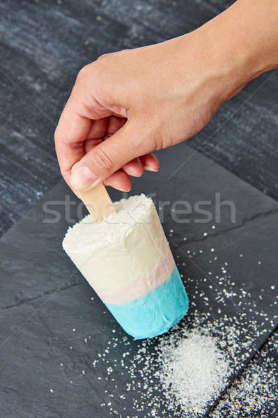 A woman's hand holds a coconut ice cream on a stick on a black slate board, with a coconut crumb on  Stock photo © artjazz