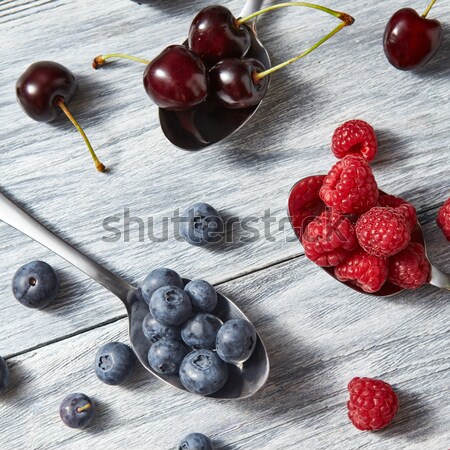 Stock photo: Freshly picked raspberry and blueberry in a spoons on a gray wooden background. Top view.