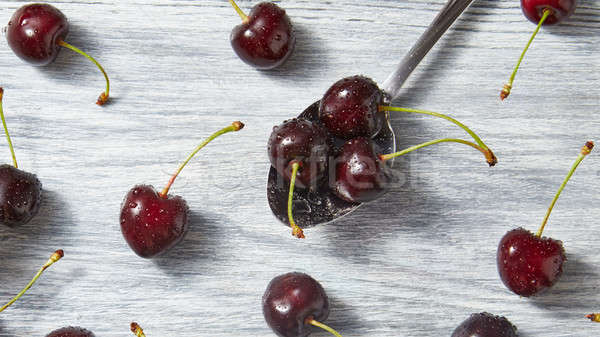 The spoon with juicy ripe cherries in water droplets with berries on a gray wooden background. Stock photo © artjazz