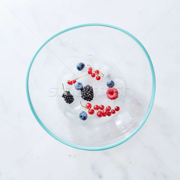 Glass bowl with different fresh berries and ice cubes on a gray marble background with space for tex Stock photo © artjazz