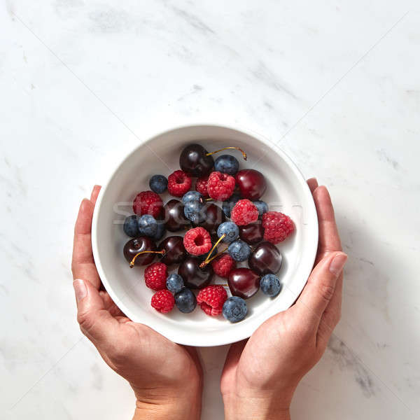 Women's hands hold a plate with ripe sweet berries - cherry, raspberry, blueberries on a gray stone  Stock photo © artjazz