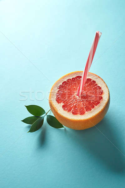 Ripe halves of grapefruit with a straw on a blue paper background Stock photo © artjazz