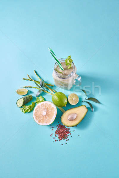Fresh juicy detox green smoothies in glass cup with green vegetables and fruits on a blue paper back Stock photo © artjazz