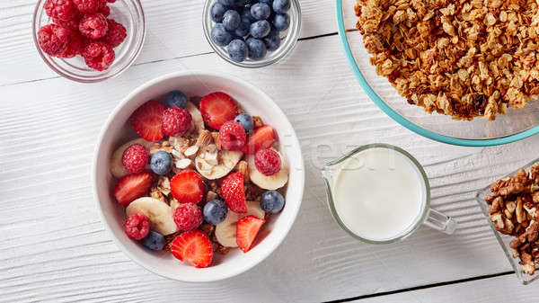 Homemade granola in a plate, sliced banana and strawberries, milk, almonds, blueberries - ingredient Stock photo © artjazz