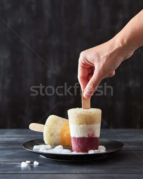Color berry ice popsicle on a stick in a black plate with pieces of ice on a black wooden background Stock photo © artjazz