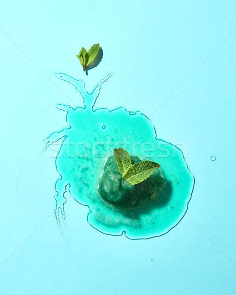 Flat lay of a puddle of melted green mint ice cream with mint leaves on a blueglass background with  Stock photo © artjazz