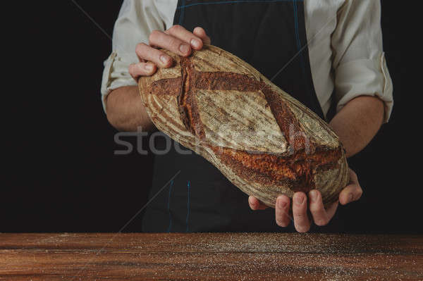 Baker's hands hold an oval bread. Stock photo © artjazz