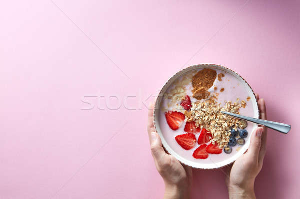 Stock photo: Woman's hands holding a bowl of organic yogurt smoothie with strawberries, banana, blueberry, oat fl