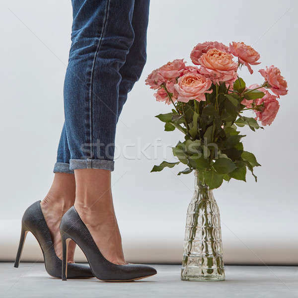 A beautiful bouquet of pink roses in a glass vase on the floor next to a girl's legs in jeans Stock photo © artjazz