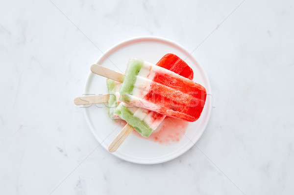 A stack of berry melting ice cream lolly in a white plate on a gray marble background, a copy of the Stock photo © artjazz