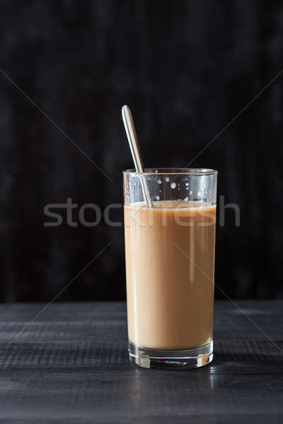 Delicious coffee with milk in a glass with a spoon on a black wooden table with copy space Stock photo © artjazz