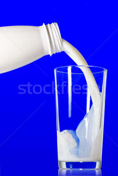 Milk pouring from bottle into glass on blue background Stock photo © artjazz