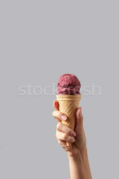 A woman's hand holds a waffle cone with red cherry sorbet on a light gray background. Stock photo © artjazz