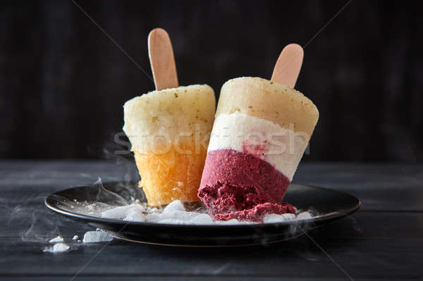 Berry sorbet lolly on a stick in a plate with slices of ice on a black wooden background. Dietary de Stock photo © artjazz