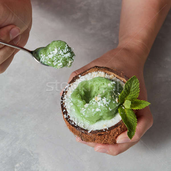 Girl holding spoon with mint ice cream and half of coconut shell Stock photo © artjazz