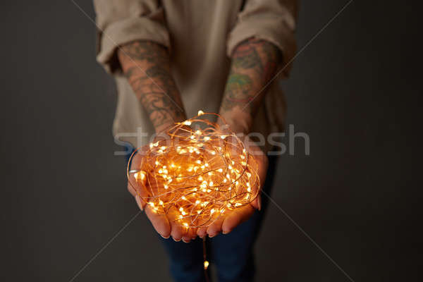 Female hands with tattoos hold yellow garlands on a dark background. Layout for postcard Stock photo © artjazz
