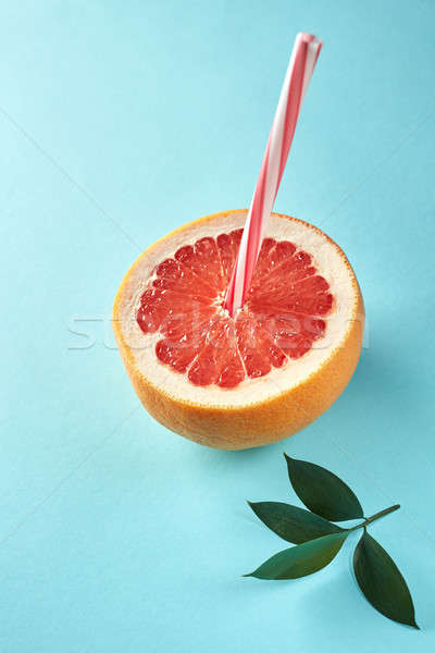Grapefruit slice with straw on pastel blue background with green leaves Stock photo © artjazz