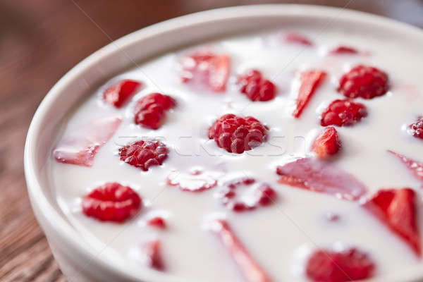 Close-up view of red ripe raspberry, pieces of strawberry with fresh milk in a bowl on a wooden tabl Stock photo © artjazz