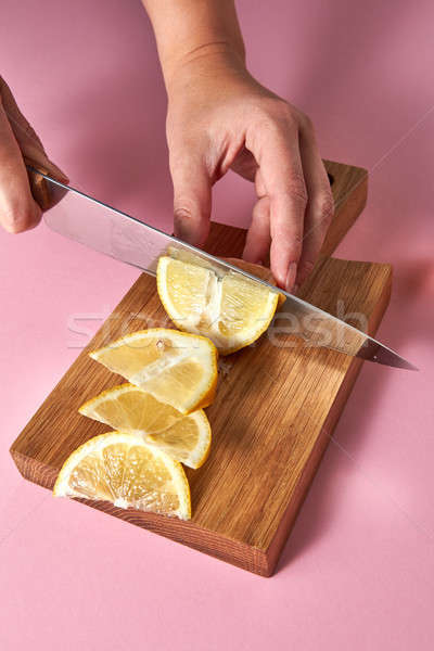 Woman cutting organic yellow ripe lemon with steel knife on pink for preparation detox drink for die Stock photo © artjazz
