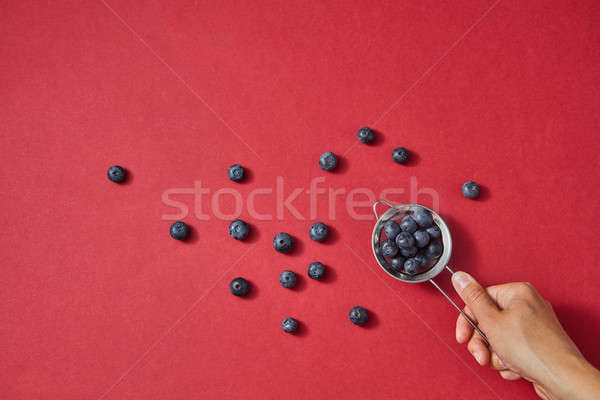 A womens hand holds a colander with red ripe sweet blueberry on a red paper background. Stock photo © artjazz